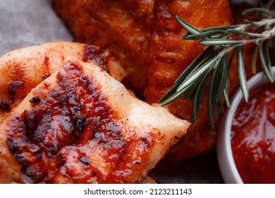 Grilled Piece Of Meat. Crispy Chicken Wings. The Texture Of The Meat Is Very Close Up. Seasoning In The Form Of Ketchup And Sprigs Of Rosemary.