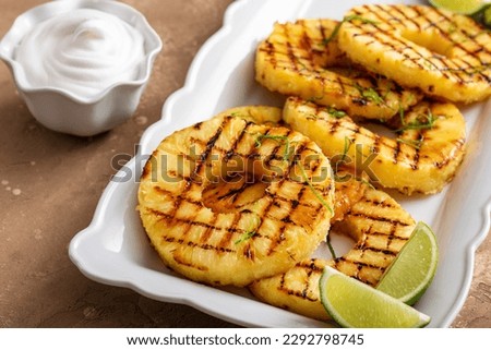 Grilled pineapple with lime honey glaze, lime zest and whipped cream on a serving plate
