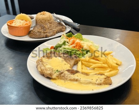 Grilled pork chop steak topped with melted cheese serve with frenchfrie and vegetables.