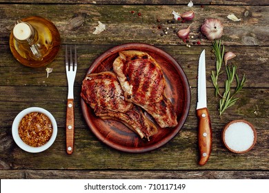 Grilled Pork Chops In A Plate With Fork And Knife On An Old Wooden Table. Top View, Flat Lay.