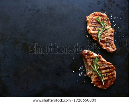 Grilled pork loin on a bone on a black metal background. Top view with copy space.