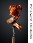 Grilled pork ribs on a fork. Grilled meat sprinkled with rosemary on a black background.