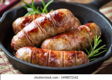 Grilled pork sausages or bangers in cast iron skillet or frying pan with tomatoes, garlic and rosemary