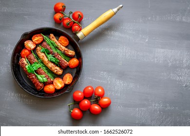 Grilled pork sausages or bangers in cast iron skillet or frying pan with tomatoes with dill and green onions