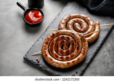 Grilled pork sausages with sauce on black stone board on dark background. BBQ. Homemade Snail round sausage. Copy space.