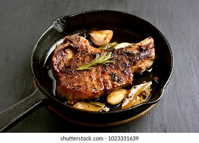Grilled pork steak in frying pan on black stone table, close up view