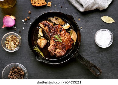 Grilled pork steak in frying pan over dark background, top view