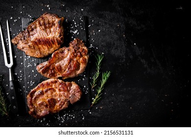Grilled pork steak with a sprig of rosemary. On a black background. High quality photo