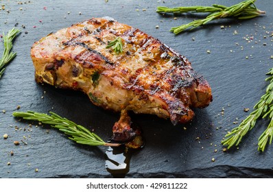 Grilled pork steaks and rosemary on black stone background