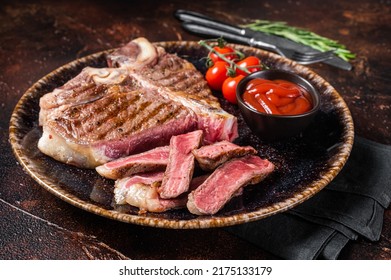 Grilled porterhouse beef meat Steak, cooked t bone in a plate with tomato. Dark background. Top view. - Shutterstock ID 2175133179