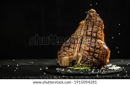 Grilled Premium Dry Aged T-bone Steak or porterhouse steak adding salt in a freeze motion on black background. USDA Prime Beef. Restaurant menu, cookbook recipe. Long banner format. Stock foto © 