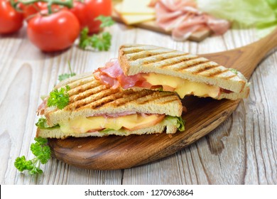 gegrillter und gepresster Toast mit geräuchertem Schinken, Käse, Tomaten und Salat auf Holzbrett