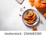 Grilled pumpkin slices with garlic and herbs on white background, copy space. Oven baked pumpkin, seasonal autumn side dish or vegan meal.