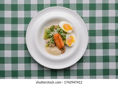 Grilled red fish steak and boiled eggs served in a white plate over green plaid tablecloth. Italian cuisine, Italian concept. Tasty dinner. Sea food.