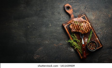 Grilled ribeye beef steak, herbs and spices on a dark table. Top view. Free space for your text. - Shutterstock ID 1411439009
