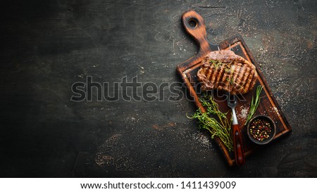 Grilled ribeye beef steak, herbs and spices on a dark table. Top view. Free space for your text.