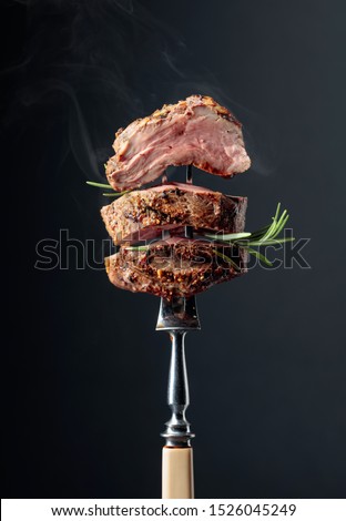 Grilled ribeye beef steak with rosemary on a black background.  Beef steak on a fork.