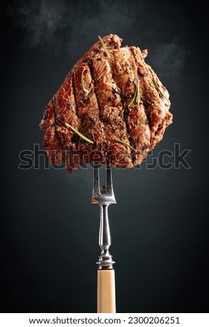 Grilled ribeye beef steak with rosemary on a black background. Beef steak on a fork sprinkled with rosemary. 