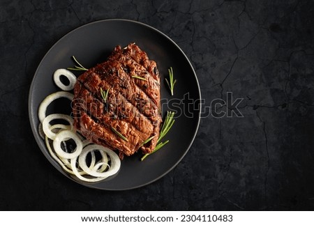 Grilled ribeye beef steak with rosemary and marinated onion on a black stone table. Copy space.