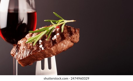 A grilled rib-eye beef steak seasoned with rosemary and accompanied by red wine, all set against a black background. The steak, perched on a fork,is garnished with rosemary and sprinkled with sea Salt - Powered by Shutterstock