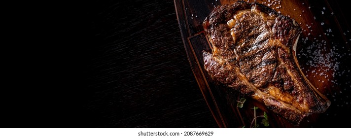 Grilled Ribeye Steak on bones on wooden board, prime cowboy steak on dark background - Shutterstock ID 2087669629