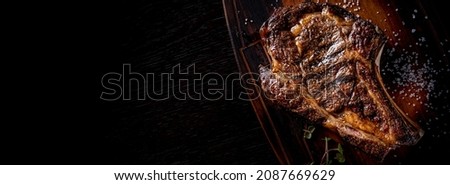 Grilled Ribeye Steak on bones on wooden board, prime cowboy steak on dark background