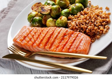 Grilled Salmon Fillet, Roast Brussel Sprouts And Boiled Farro On A White Plate  With Golden Cutlery, Healthy Diet