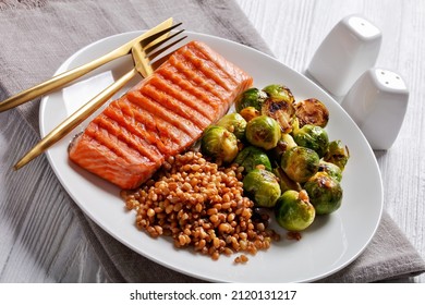 Grilled Salmon Fillet, Roast Brussel Sprouts And Boiled Farro On A White Plate  With Golden Cutlery