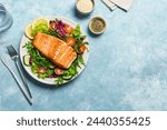 Grilled salmon fish fillet and fresh vegetable salad. Healthy keto food - green salad and roasted salmon on blue background, copy space. Barbecue meal.