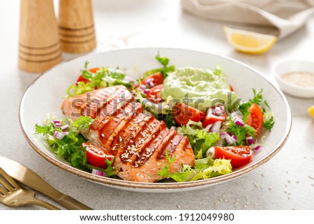 Grilled salmon fish fillet and fresh green lettuce vegetable tomato salad with avocado guacamole.