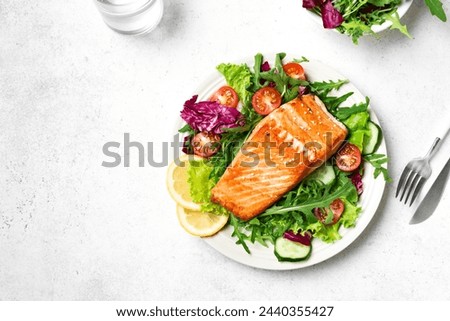 Grilled salmon fish fillet and fresh vegetable salad. Healthy keto food - green salad and roasted salmon steak on white background, top view, copy space. Barbecue meal.