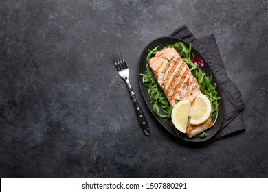 Grilled Salmon Fish Fillet With Salt, Pepper And Rosemary Over Salad Leaves. On Stone Table With Copy Space. Top View Flat Lay 