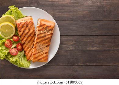 Grilled salmon with lemon, tomato on the wooden background. Copyspace for your text.