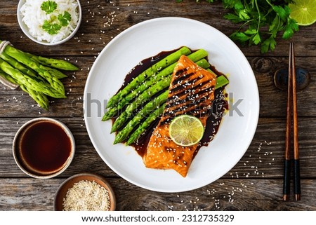 Grilled salmon steak with green asparagus in teriyaki sauce on wooden table 