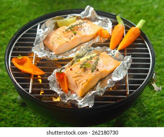 Grilled Salmon Steaks With Baby Vegetables Cooking On Tin Foil Over A Barbecue Outdoors In Summer With Baby Carrots And Sweet Pepper