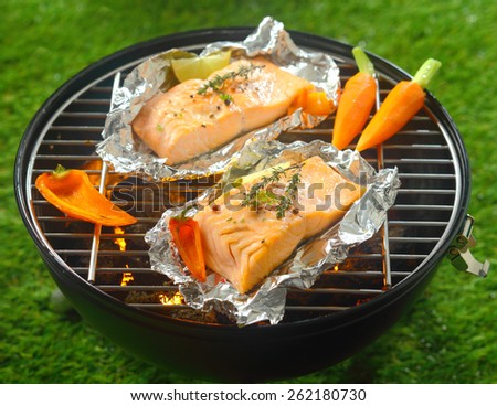 Grilled salmon steaks with baby vegetables cooking on tin foil over a barbecue outdoors in summer with baby carrots and sweet pepper