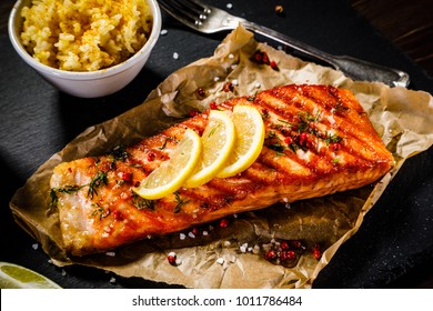Grilled salmon with vegetables served on black stone plate on wooden table 