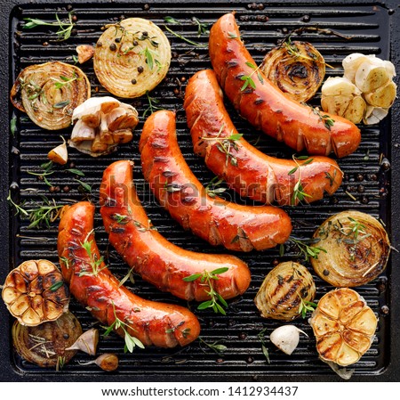 Grilled sausage with the addition of herbs and vegetables on the grill plate, outdoors. Grilling food, bbq, barbecue