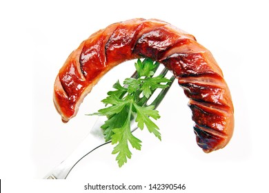 grilled sausage with parsley leaves on a metal fork, white background.