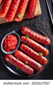 Grilled sausages with ketchup, overhead flat lay shot on a black slate background. Spicy Bratwurst