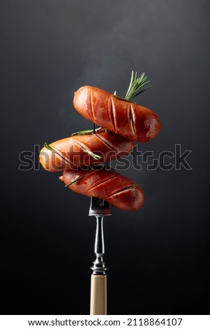 Grilled sausages with rosemary on a fork.