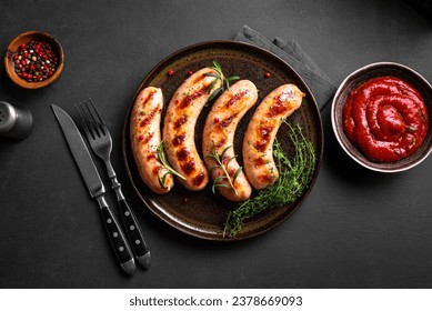 Grilled sausages with tomato sauce and herbs on black background, top view, copy space. Roasted homemade german wurst sausages on plate.