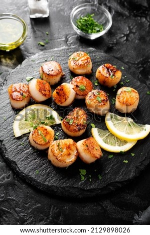 Grilled scallops with creamy lemon spicy sauce on black background.