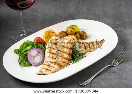 Grilled sea bass fillet with salad and potatoes on stone table