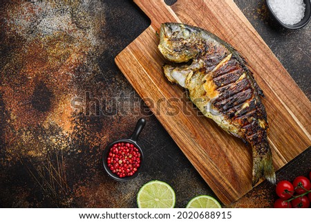 Grilled sea bream or dorado raw fish on chopping  board with ingredients over old metall dark background, top view with space for text