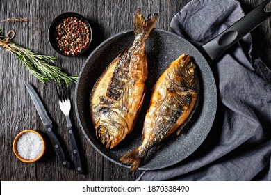 Grilled Sea Bream, Orata, Dorado Fish In A Skillet On A Dark Wooden Table With A Fork, Rosemary And Peppercorn, Horizontal View From Above, Flat Lay