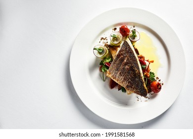 Grilled seabass with vegetables top view, close-up, white plate, light background, copy space