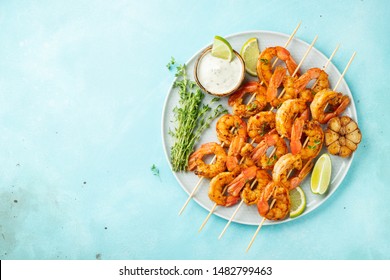 Grilled Shrimp Skewers Or Langoustines Served With Lime, Garlic And Sauce On A Light Blue Concrete Background. Seafood. Top View With Copy Space. Flat Lay