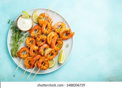 Grilled Shrimp Skewers Or Langoustines Served With Lime, Garlic And Sauce On A Light Blue Concrete Background. Seafood And Beer. Top View With Copy Space. Flat Lay