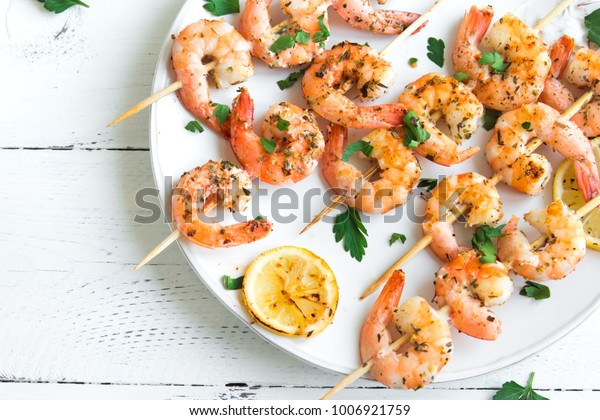 Grilled shrimp skewers. Seafood, shelfish.\
Shrimps Prawns skewers with spices and fresh herbs on white wooden\
background, copy space. Shrimps prawns brochette kebab. Barbecue\
srimps prawns.